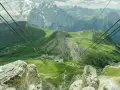 Vista mozzafiato da Canazei al Passo Sella, con funivia che attraversa verdi pendii e imponenti vette dolomitiche.