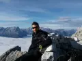 Uomo in vetta con abbigliamento tecnico, ideale per capire come vestirsi in montagna a settembre. Paesaggio alpino mozzafiato.