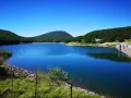 Vasto lago di Comano con acque blu intenso, circondato da colline verdi e una diga in cemento.