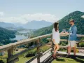 Coppia brinda con vino su un balcone con vista sulla **montagna di Pinè** e laghi.