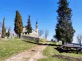 A church with a bell tower sits on a grassy hill, with tall trees and a picnic table in the foreground.