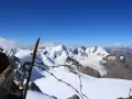 Vista mozzafiato dalla punta Linke, con cime innevate e un cielo azzurro intenso. Un vecchio piccone arrugginito e filo spinato segnano il confine.
