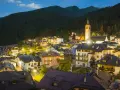 Villaggio alpino di Ossana, Val di Sole, illuminato di notte, con case colorate e una chiesa con campanile che svetta tra i boschi.