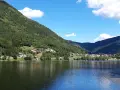 Il **lago di Serraia** riflette le montagne boscose e un villaggio alpino sotto un cielo azzurro con nuvole bianche.
