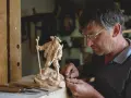 Maestro intaglia un pastore con bastone, un esempio di artigianato legno trentino.