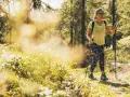 Una donna con bastoncini da trekking cammina su un sentiero soleggiato in Trentino, godendosi un facile trekking tra i boschi.