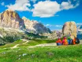 Quattro escursionisti ammirano un maestoso itinerario dolomiti, con cime imponenti e un rifugio alpino.