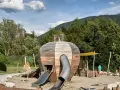 Un colorato parco giochi Trentino con una struttura a forma di sfera in legno, scivoli e bambini che giocano.
