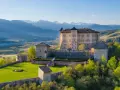 Castelli Val di Non, un imponente maniero su una collina verdeggiante, con montagne innevate sullo sfondo.