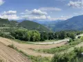 Panoramica del passo di Santa Barbara a Trento, con campi coltivati, alberi verdi e montagne sullo sfondo.