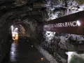 Un suggestivo tunnel roccioso illuminato, con un cartello che recita "Suoni voci della Guerra Bianca". Un percorso che sembra condurre alla galleria paradiso.