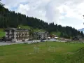 Edifici alpini e un campo da calcio con porte, immersi nel verde e circondati da boschi. La **passo Cereda altitudine** offre uno scenario incantevole.