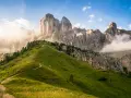 Sentiero serpeggiante su un prato verdeggiante ai piedi di un imponente gruppo montuoso tra Veneto e Trentino Alto Adige, con nuvole che accarezzano le cime rocciose.