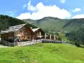 Rifugio in legno con tavoli all'aperto, ideale per un giro delle malghe in Val di Non. Montagne verdi e cielo azzurro.