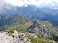 Panoramica mozzafiato del **Passo Pordoi** con strade tortuose che si snodano tra verdi pendii e imponenti vette rocciose, sotto un cielo nuvoloso.