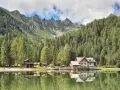Riflessi sul lago alpino nella piana di Nambino, con boschi di conifere e montagne sullo sfondo.