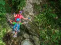 Bambini affrontano un emozionante percorso ponte tibetano tra rocce e vegetazione lussureggiante.