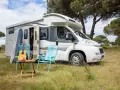 Un camper pronto per un tour in Trentino, con chitarra, cappello e sedie da campeggio in un prato verde.