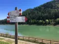 Cartello con indicazioni per Tavon di Coredo, Merlonga e Sfruz, con lago verde e bosco sullo sfondo.