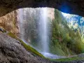 Vista da una grotta su maestose cascate del Trentino, con sentieri e ponticelli che invitano all'esplorazione.
