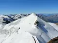 Alpinisti in cammino sulla cresta innevata del ghiacciaio Cevedale, con vette maestose sullo sfondo.