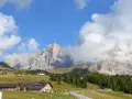Panorami mozzafiato per escursioni a Passo Rolle. Rifugi alpini e vette imponenti sotto un cielo azzurro con nuvole bianche.