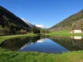 I laghetti di Vermiglio riflettono montagne innevate e un cielo azzurro. Un edificio moderno si specchia nell'acqua calma.