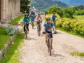 Gruppo di ciclisti su sentiero sterrato, godendosi gli eventi Trentino in un paesaggio verdeggiante.