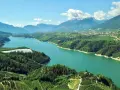 Panoramica mozzafiato del lago di Santa Giustina, circondato da verdi colline coltivate e montagne imponenti.