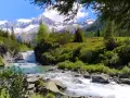 Un torrente impetuoso scorre tra rocce e vegetazione lussureggiante nel **Val di Fumo**, con montagne innevate sullo sfondo.