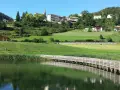Una piacevole passeggiata dria al fos, con un ponte di legno che attraversa il lago e un villaggio sullo sfondo.