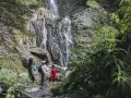Escursionisti ammirano le spettacolari cascate schiavaneis, immerse nel verde e circondate da rocce basaltiche.