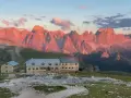 Rifugio sul **Monte Catinaccio** illuminato dal tramonto, con le vette rocciose che si tingono di rosa.
