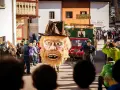 Gigantesca maschera pelosa con cappello marrone sfila al carnevale trentino. Un uomo con maschera grottesca trascina una catena.