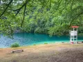 Rilassante **lago Lamar** con acque turchesi, bagnanti e torretta di salvataggio sotto alberi verdi.