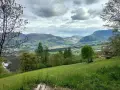 Prato verde e montagne sullo sfondo nella valle di Comano. Una casa con tetto in legno e un albero solitario.