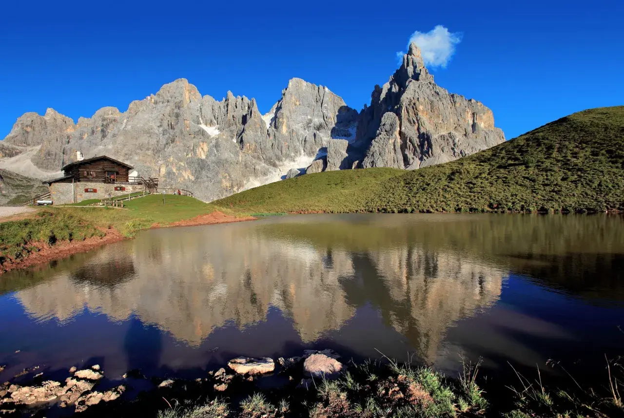 Riflessi maestosi delle cime nel lago di Val Venegia, con un rifugio alpino in primo piano.