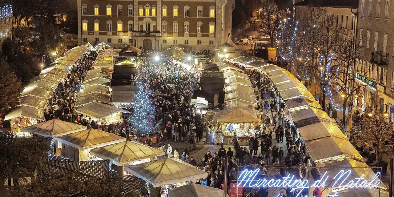Un affollato Mercatino di Natale a Trento, con bancarelle illuminate, un albero scintillante e gente che passeggia tra le luci festive.