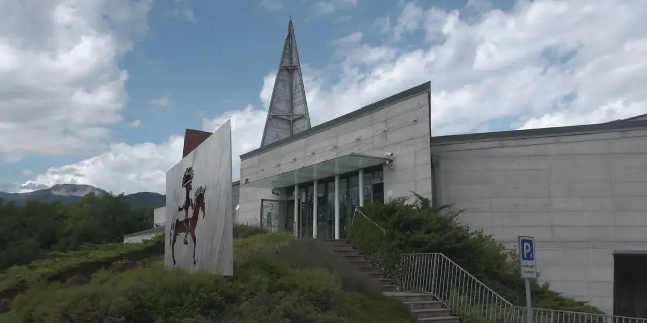 Il museo retico, con la sua architettura moderna e un'installazione artistica di un guerriero a cavallo, si erge sotto un cielo nuvoloso.