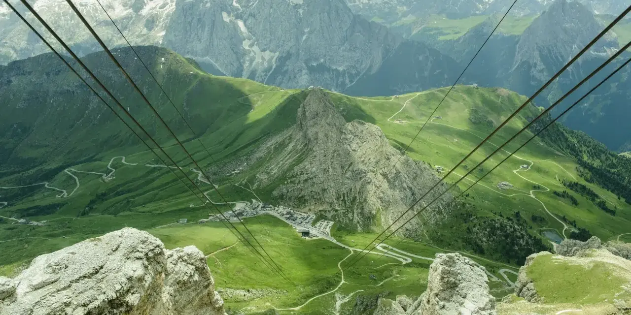 Vista mozzafiato da Canazei al Passo Sella, con funivia che attraversa verdi pendii e imponenti vette dolomitiche.