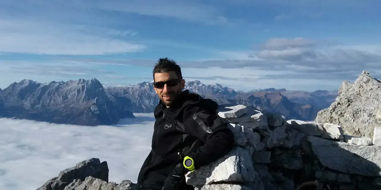 Uomo in vetta con abbigliamento tecnico, ideale per capire come vestirsi in montagna a settembre. Paesaggio alpino mozzafiato.