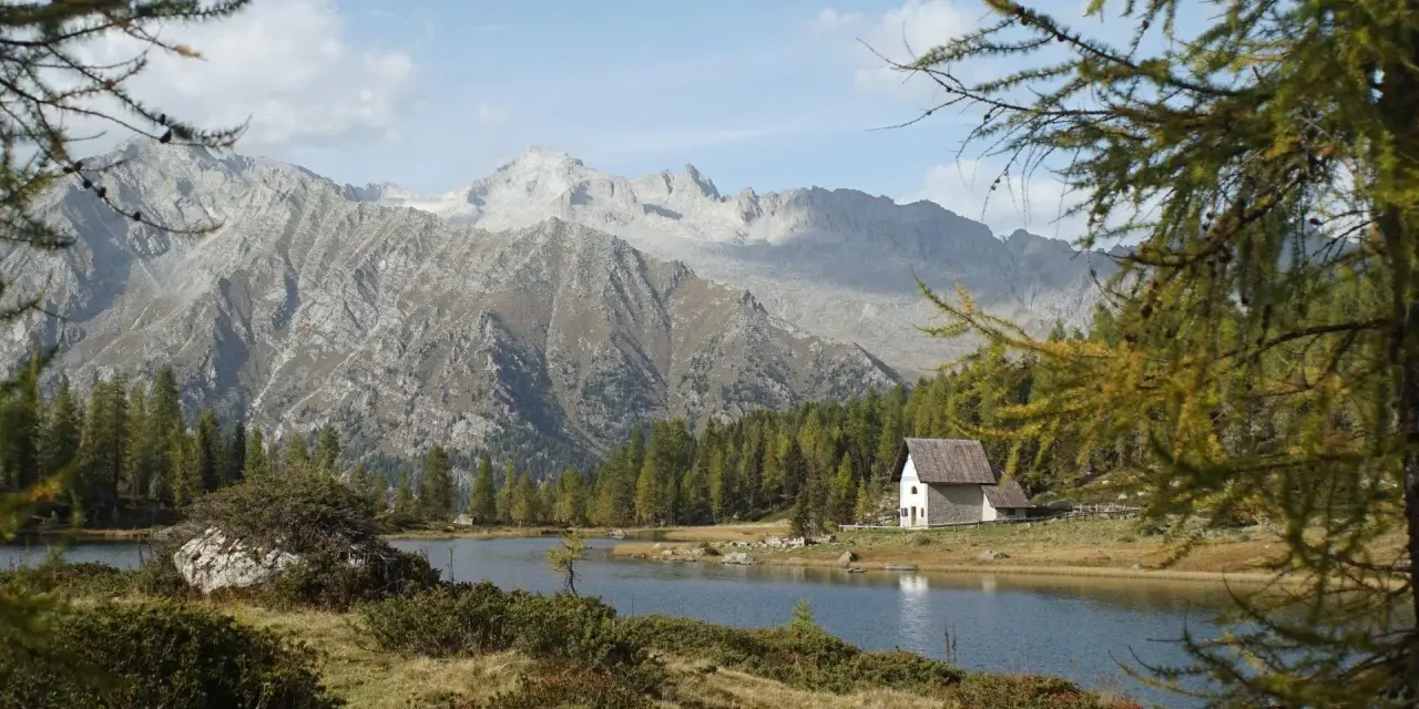 Un rifugio solitario si specchia nei laghi di San Giuliano, circondato da boschi e imponenti montagne.