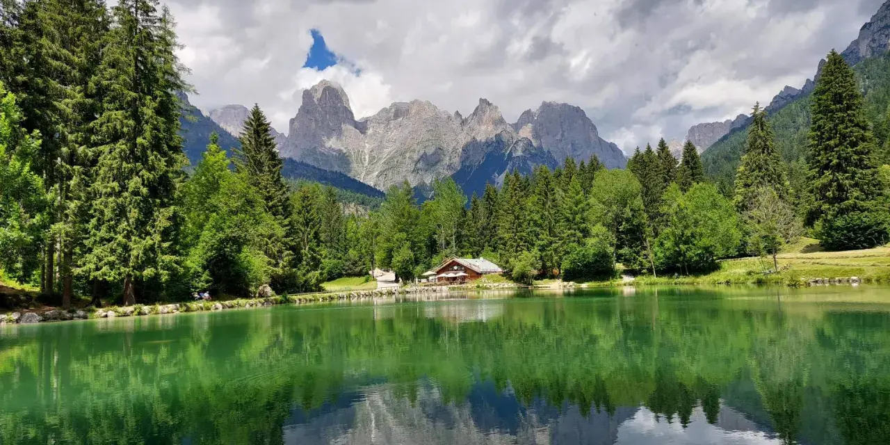 Riflessi alpini sul lago di Passo Cereda. Montagne imponenti e boschi verdi incorniciano un tranquillo specchio d'acqua.