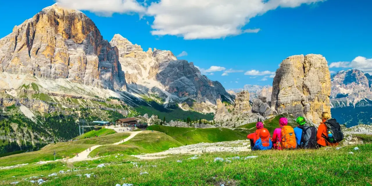 Quattro escursionisti ammirano le maestose Dolomiti Trentino Alto Adige, con cime imponenti e un cielo azzurro.