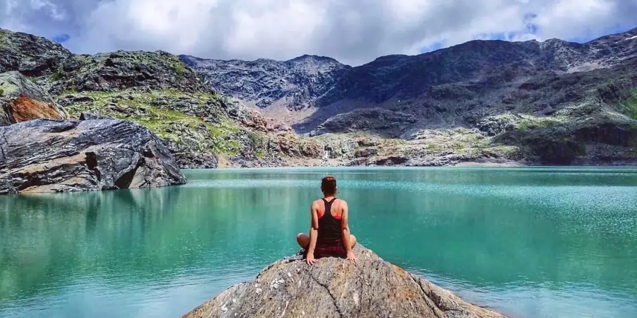 Donna seduta su una roccia ammira il **lago del Carest** con le montagne sullo sfondo.