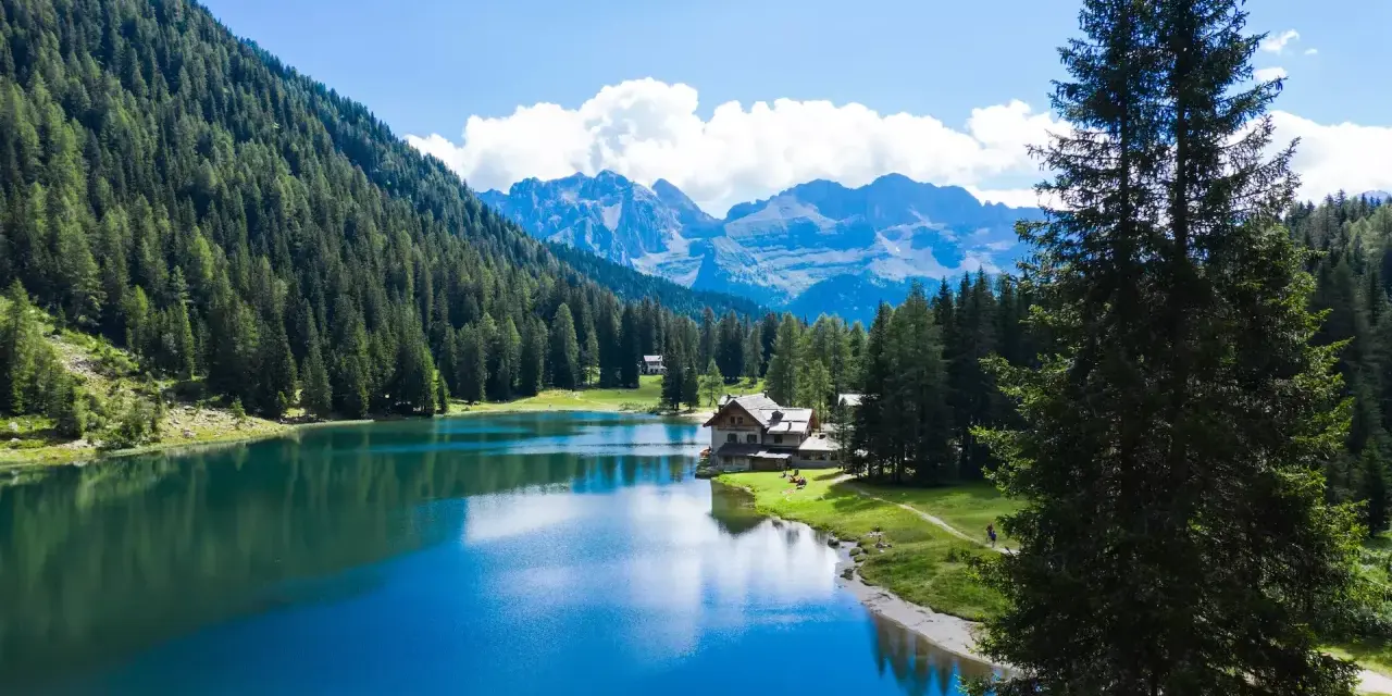 Incantevole lago alpino vicino a Madonna di Campiglio, con boschi rigogliosi, montagne maestose e un rifugio accogliente.