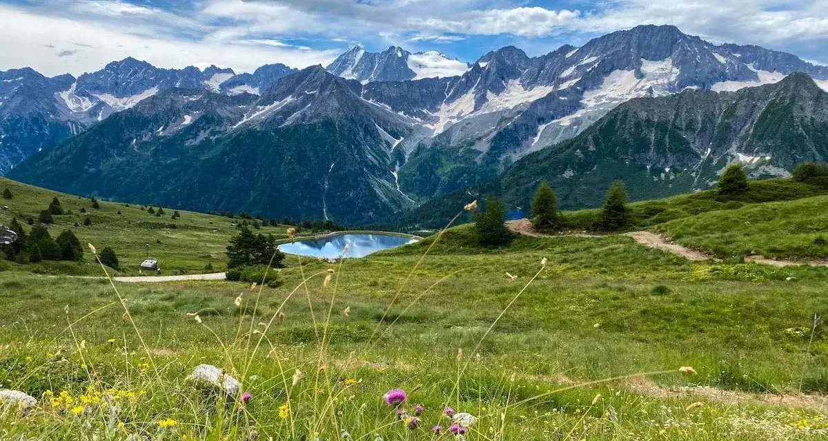Un incantevole passo tra Lombardia e Trentino, con un lago alpino specchiato e montagne innevate sullo sfondo.