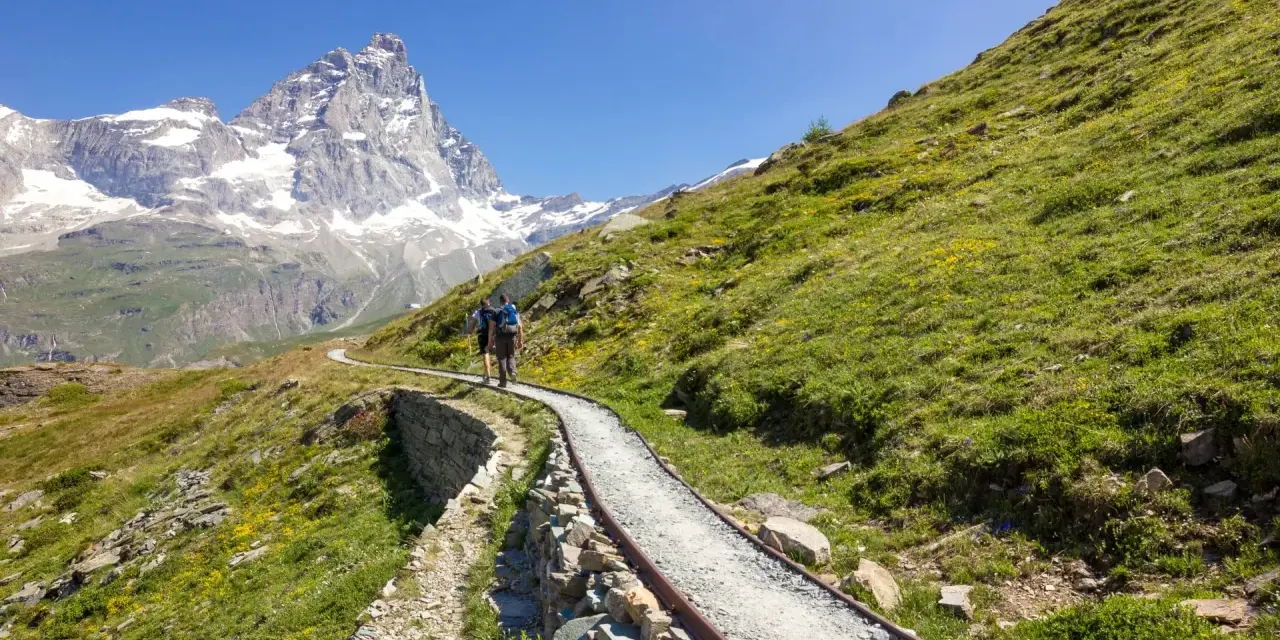 Due escursionisti affrontano un sentiero panoramico, con il Cervino innevato sullo sfondo, durante un **trekking due giorni Dolomiti**.