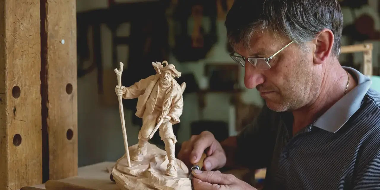 Maestro intaglia un pastore con bastone, un esempio di artigianato legno trentino.