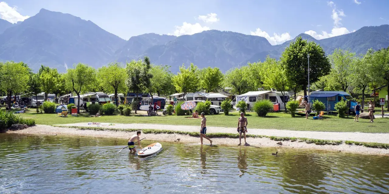 Giovani si godono il lago di Levico spiaggia, con campeggio e montagne sullo sfondo.